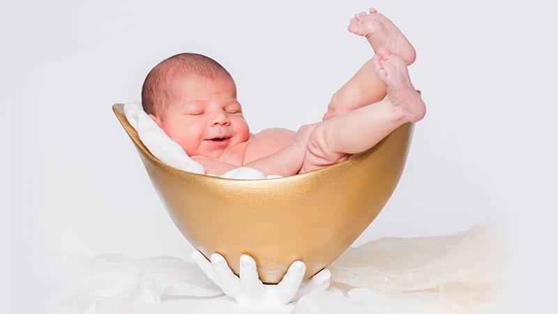Ein Baby in einer goldenen Belly Bowl, die von zwei Gips Händen gehalten wird.