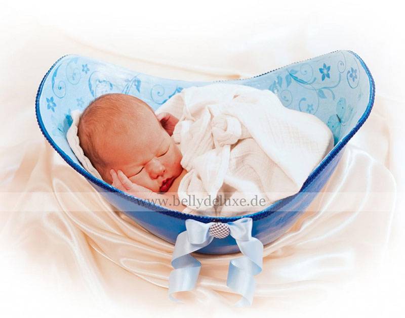 Ein Neugeborenes in einer mit blauer Farbe angemalten und mit Motivfolie verzierten Babyschale.