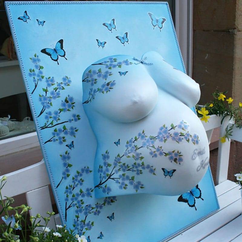 Blauer Babybauchabdruck mit Schmetterlingen und Blüten über die Holzplatte und Bauch gemalt