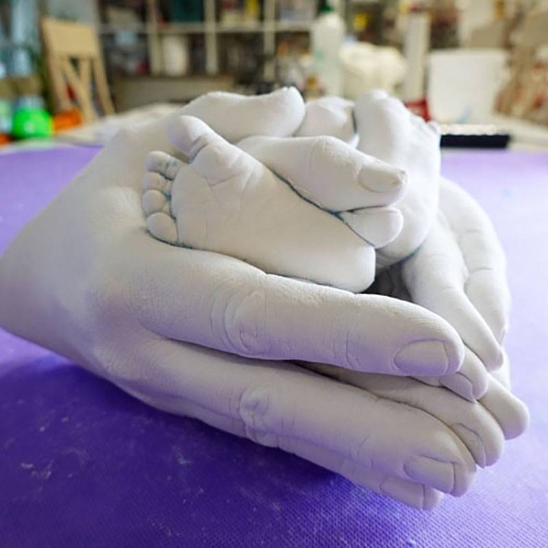 3D Familiengipsabdruck von den Händen der Eltern, die, die Füße des Babys festhalten.
