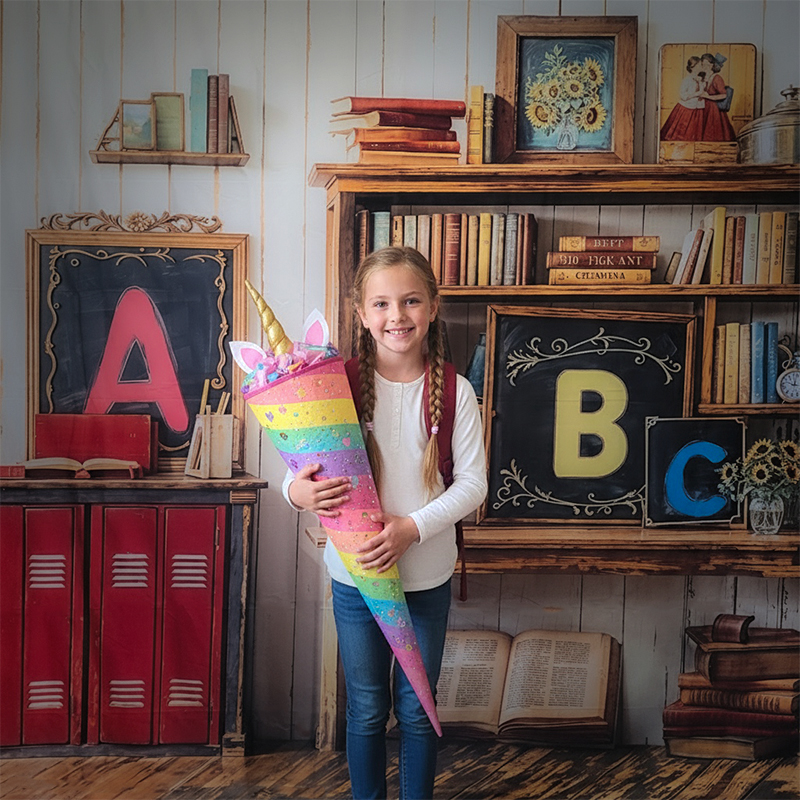 Ein Mädchen mit geflochtenen Zöpfen hält eine bunte Einhorn-Schultüte und lächelt fröhlich vor einer Kulisse mit großen Buchstaben, Büchern und Schulmotiven – perfekte Erinnerung zur Einschulung in Karlsruhe.
