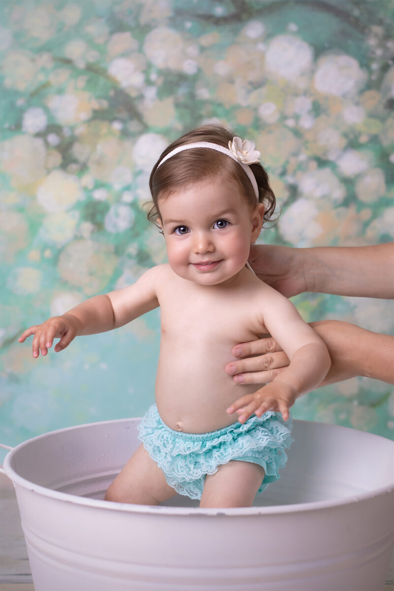 Kind steht in einer weißen Wanne im Fotostudio, wird von Händen gestützt und lächelt in die Kamera.