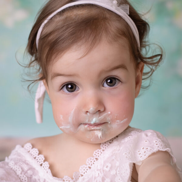 Lustiges Cake-Smash-Fotoshooting in Karlsruhe – Nahaufnahme eines Babys mit Tortencreme im Gesicht und Stirnband.
