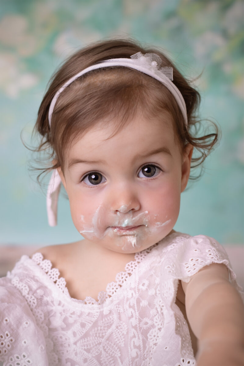 Lustiges Cake-Smash-Fotoshooting in Karlsruhe – Nahaufnahme eines Babys mit Tortencreme im Gesicht und Stirnband.