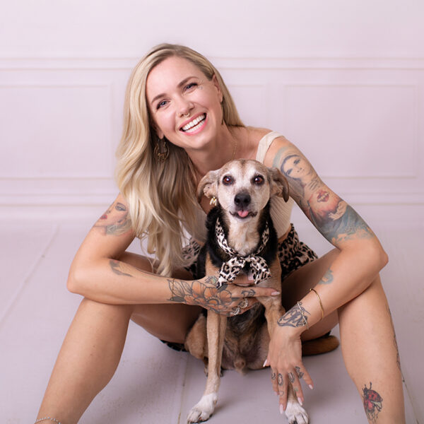Frau sitzt im Fotostudio auf dem Boden und hält ihren Hund im Arm, beide schauen freundlich in die Kamera.
