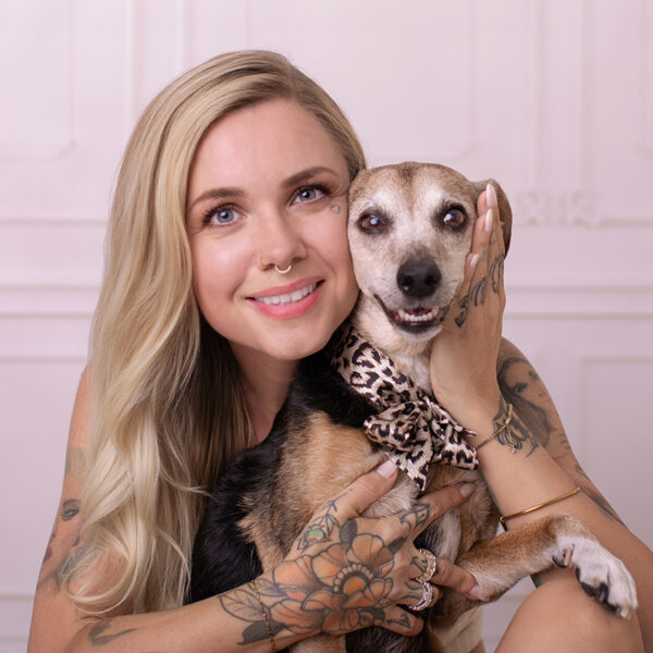 Frau kuschelt im Studio mit ihrem Hund und lächelt in die Kamera, helles Hintergrundset.