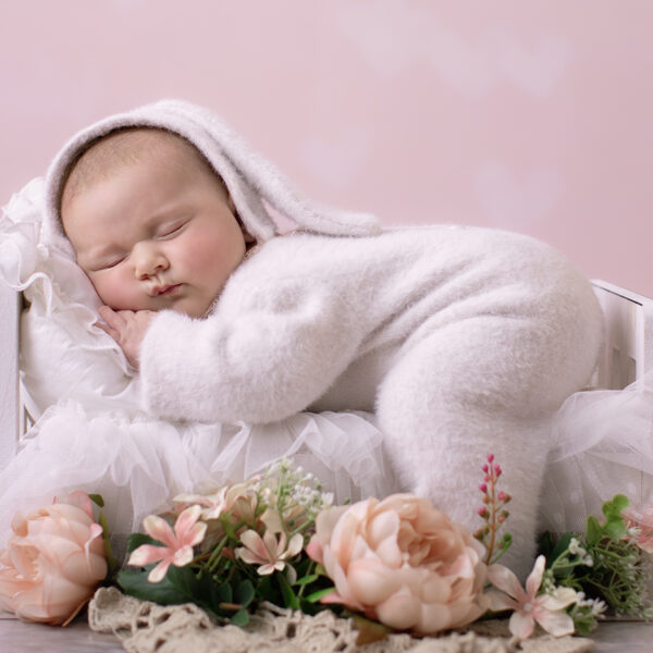 Neugeborenes Baby im Fotostudio liegend auf einem Mini Bett mit Blumendekoration