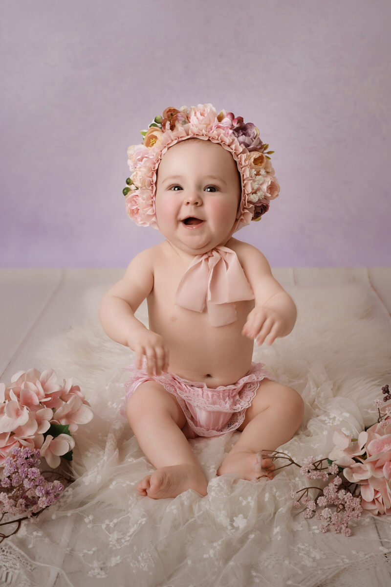 Baby mit Haarband sitzt im Studio und schaut neugierig in die Kamera.