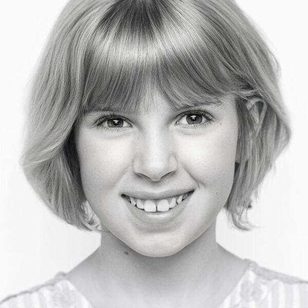 Schwarzweiß-Portrait eines lächelnden Mädchens vor weißem Hintergrund, schlicht und ausdrucksstark im Pure-Beauty-Stil.