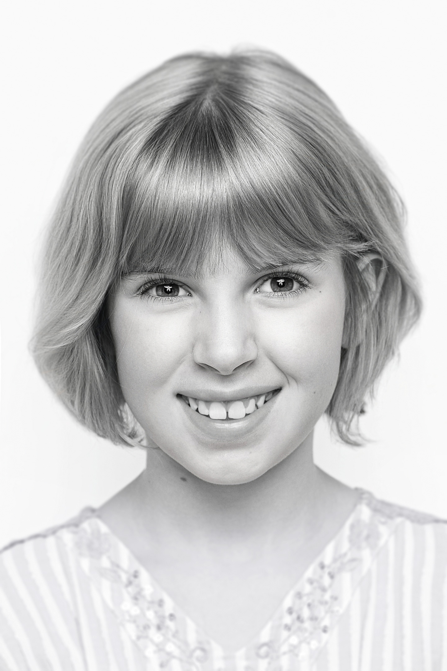 Schwarzweiß-Portrait eines lächelnden Mädchens vor weißem Hintergrund, schlicht und ausdrucksstark im Pure-Beauty-Stil.