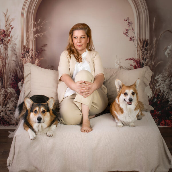 Gemütliches Boho-Mini-Shooting in Karlsruhe mit zwei Corgis und Halterin auf einem beigen Tagesbett vor einer Trockenblumenkulisse.