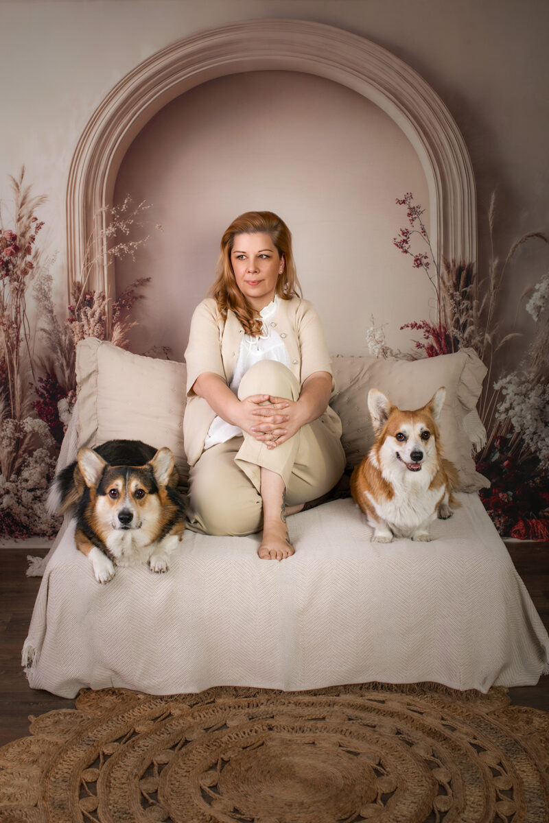 Gemütliches Boho-Mini-Shooting in Karlsruhe mit zwei Corgis und Halterin auf einem beigen Tagesbett vor einer Trockenblumenkulisse.