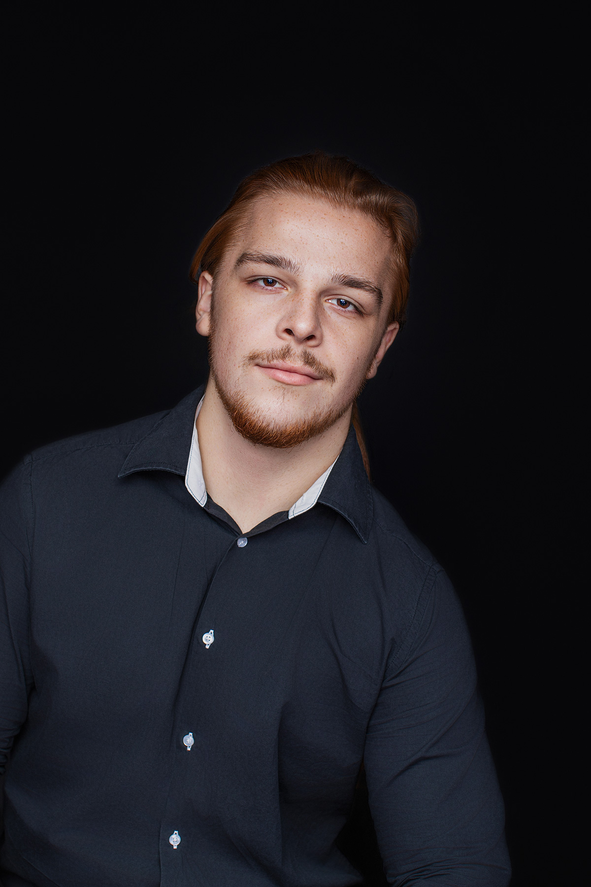 Nahaufnahme Charakterporträt eines jungen Mannes mit Bart vor dunklem Hintergrund fotografiert im Fotostudio Karlsruhe