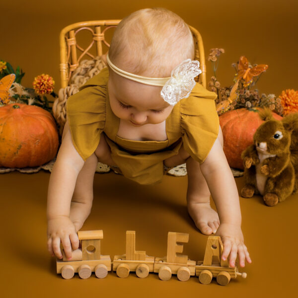 Baby im Herbst-Set spielt mit Holzspielzeug im Studio.