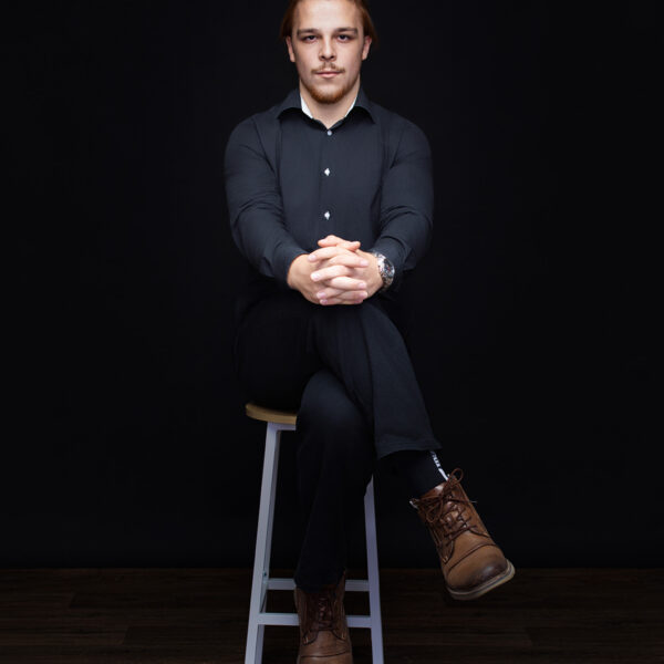 Professionelles Personal Branding Porträt sitzend auf einem Barhocker vor schwarzem Studiohintergrund in Karlsruhe