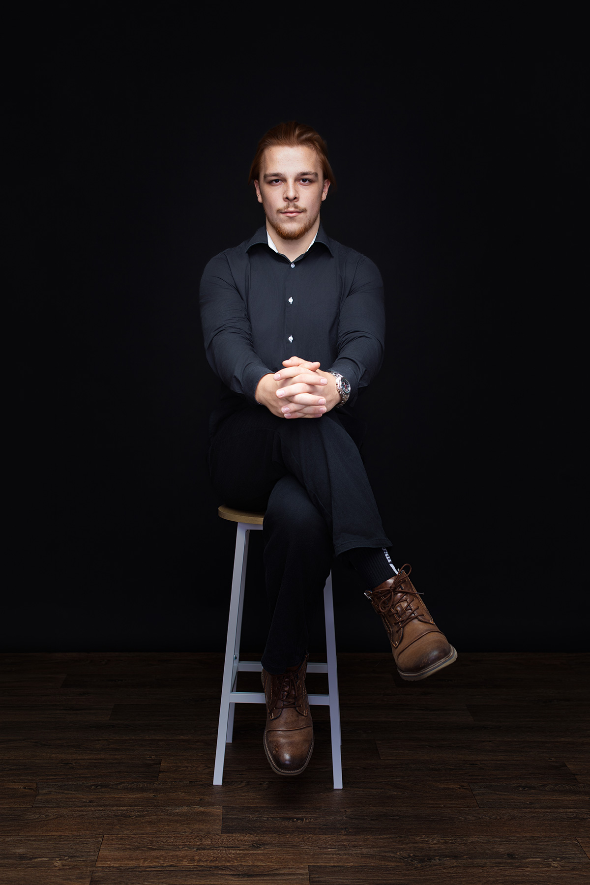 Professionelles Personal Branding Porträt sitzend auf einem Barhocker vor schwarzem Studiohintergrund in Karlsruhe