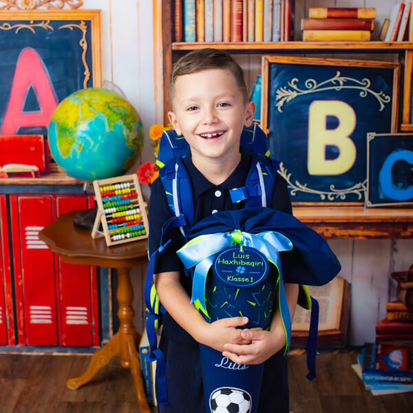 Junge lächelt beim Fotoshooting mit blauer Schultüte